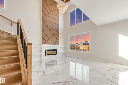 Two-story living area featuring a modern fireplace with a marble-look surround, a decorative wood-paneled accent wall, and built-in shelving - 4015 39 Street, Beaumont, AB - Indoor Photo Showing Other Room