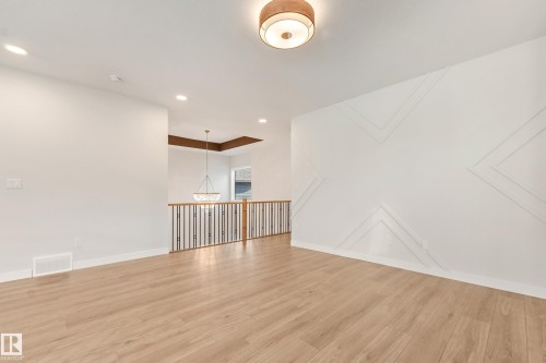 Spacious room featuring wood-finish flooring and a decorative accent wall with geometric paneling - 4015 39 Street, Beaumont, AB - Indoor Photo Showing Other Room