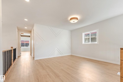 Spacious room featuring light wood-finish flooring, a decorative accent wall with geometric molding, and a contemporary flush-mount ceiling light - 4015 39 Street, Beaumont, AB - Indoor Photo Showing Other Room