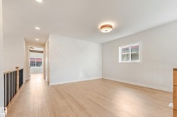 Spacious room featuring light wood-finish flooring, a decorative accent wall with geometric molding, and a contemporary flush-mount ceiling light - 