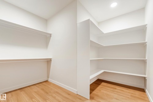 Spacious walk-in closet featuring wood-finish flooring, recessed lighting, white wall-mounted shelving, and clothing rods - 4015 39 Street, Beaumont, AB - Indoor With Storage