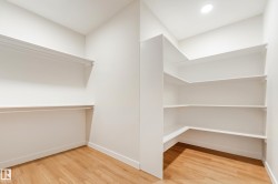 Spacious walk-in closet featuring wood-finish flooring, recessed lighting, white wall-mounted shelving, and clothing rods - 