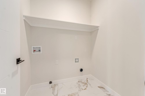 Dedicated laundry area featuring a built-in shelf, marble-patterned tile flooring, baseboard trim, and a contemporary door with matte black hardware - 4015 39 Street, Beaumont, AB - Indoor