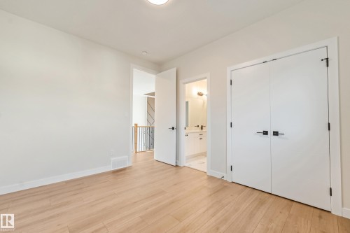 Light wood-finish flooring extending into the hallway, featuring white walls, white trim, and a white bi-fold closet door with matte black hardware - 4015 39 Street, Beaumont, AB - Indoor Photo Showing Other Room