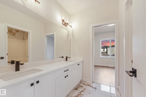 Dual vanity with matte black fixtures, white cabinetry, a light-toned countertop, and reflective flooring - 4015 39 Street, Beaumont, AB - Indoor Photo Showing Bathroom