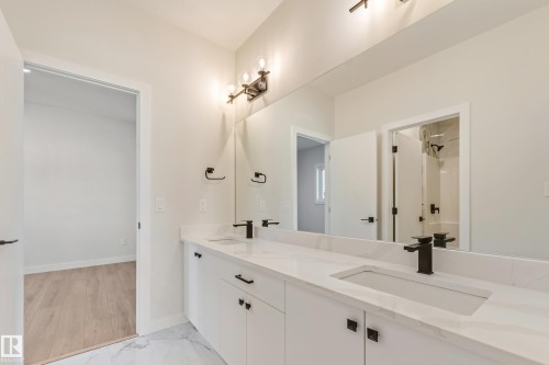 Bathroom featuring a dual vanity with integrated sinks, white cabinetry, and matte black fixtures - 4015 39 Street, Beaumont, AB - Indoor Photo Showing Bathroom