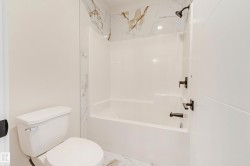 Bathroom featuring a white bathtub and shower combination with black fixtures, complemented by a white toilet - 