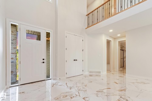 Two-story entry foyer featuring high ceilings, large format marble-look tile flooring, and a second-story overlook with a wood and wrought iron railing - 4015 39 Street, Beaumont, AB - Indoor Photo Showing Other Room