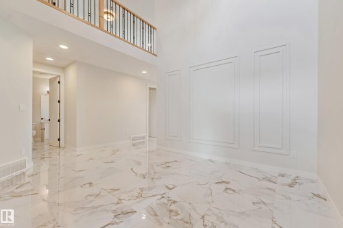 Spacious interior featuring high ceilings, large-format tile flooring, decorative wall molding, and a second-story balcony with an iron railing - 4015 39 Street, Beaumont, AB - Indoor Photo Showing Other Room