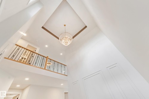 Two-story foyer with a custom chandelier, recessed lighting, a second-story landing featuring a wood handrail with black iron balusters, and wainscoting details - 4015 39 Street, Beaumont, AB - Indoor Photo Showing Other Room