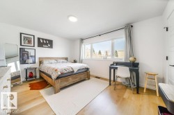 Bright bedroom featuring light wood-finish flooring, white walls, and a large multi-pane window - 