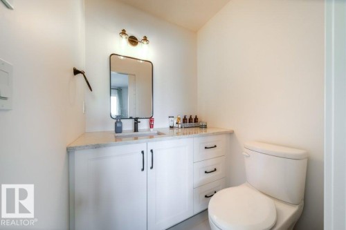 Bathroom featuring a white vanity with panel cabinetry and black hardware, a light-toned countertop, a rectangular mirror with a black frame, and a bronze-finish vanity light fixture - 11303 111 Avenue, Edmonton, AB - Indoor Photo Showing Bathroom