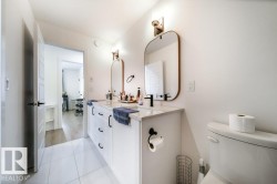 Double vanity featuring white cabinetry with black hardware, stone countertop, two rectangular mirrors, and wall-mounted sconces - 