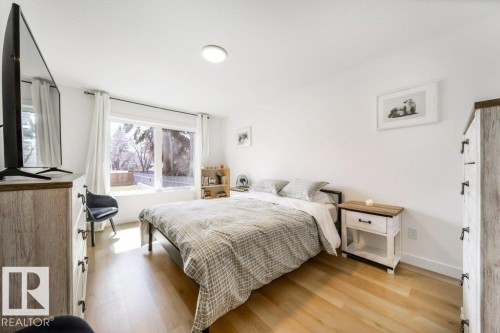 Spacious bedroom featuring light wood-finish flooring, white walls, and a large window with white curtains - 11303 111 Avenue, Edmonton, AB - Indoor Photo Showing Bedroom