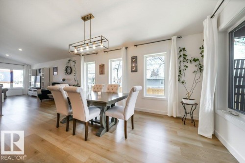 Open-concept dining area featuring light wood-finish flooring, white walls, and a contemporary linear chandelier - 11303 111 Avenue, Edmonton, AB - Indoor Photo Showing Dining Room