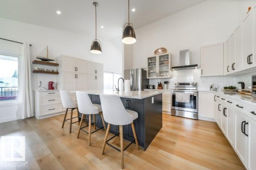 Open-concept kitchen featuring an island with counter seating, stainless steel appliances, white cabinetry with black hardware, and wood-finish flooring - 11303 111 Avenue, Edmonton, AB - Indoor Photo Showing Kitchen With Upgraded Kitchen