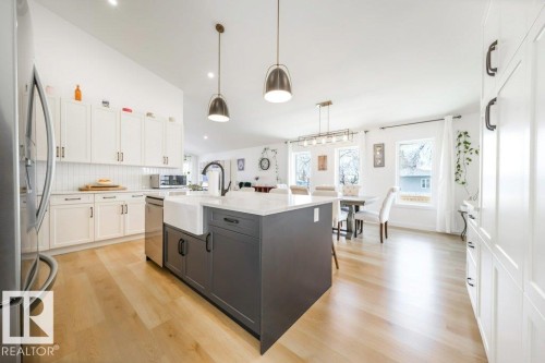 Kitchen featuring a large central island with a farmhouse sink, stainless steel appliances, white cabinetry with dark hardware, and wood-finish flooring - 11303 111 Avenue, Edmonton, AB - Indoor Photo Showing Kitchen With Upgraded Kitchen