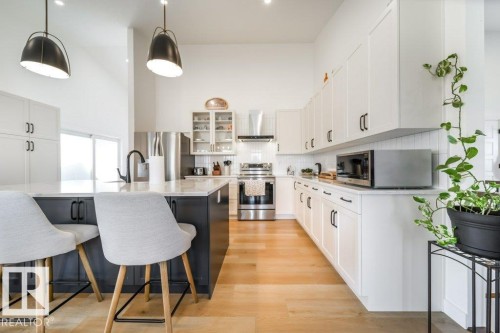 Modern kitchen featuring an expansive island with seating, white shaker cabinetry with matte black hardware, stainless steel appliances, and wood-finish flooring - 11303 111 Avenue, Edmonton, AB - Indoor Photo Showing Kitchen With Upgraded Kitchen