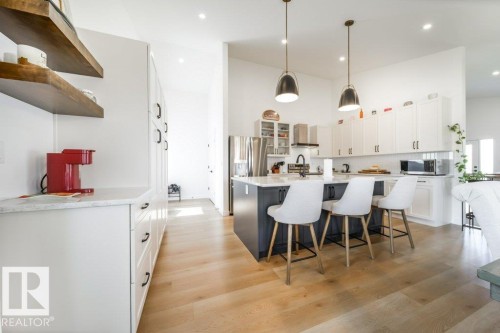 Open-concept kitchen featuring an island with seating, pendant lighting, white upper and lower cabinetry, stainless steel appliances, and light wood-finish flooring - 11303 111 Avenue, Edmonton, AB - Indoor