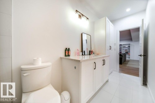 Contemporary bathroom featuring a white vanity with black hardware, stone countertop, a rectangular mirror, and an adjacent built-in storage cabinet - 11303 111 Avenue, Edmonton, AB - Indoor Photo Showing Bathroom