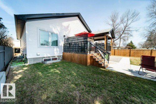Expansive backyard featuring a multi-level deck with black railings, a covered patio area, concrete pathways, and a wooden privacy fence - 11303 111 Avenue, Edmonton, AB - Outdoor