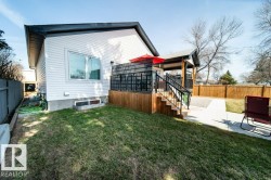 Expansive backyard featuring a multi-level deck with black railings, a covered patio area, concrete pathways, and a wooden privacy fence - 