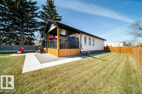 Rear exterior featuring a covered deck with dark railing, a concrete pathway, a gravel patio area, a wood fence, and a spacious lawn - 11303 111 Avenue, Edmonton, AB - Outdoor