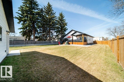 Expansive backyard featuring a large green lawn, full wooden privacy fencing, and a concrete walkway - 11303 111 Avenue, Edmonton, AB - Outdoor