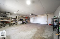 Spacious two-car garage featuring a concrete floor, built-in shelving, two overhead garage doors with automatic openers, and overhead lighting - 