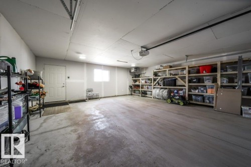 Spacious garage featuring a concrete floor, built-in wooden shelving, a window, and a white entry door - 11303 111 Avenue, Edmonton, AB - Indoor Photo Showing Garage