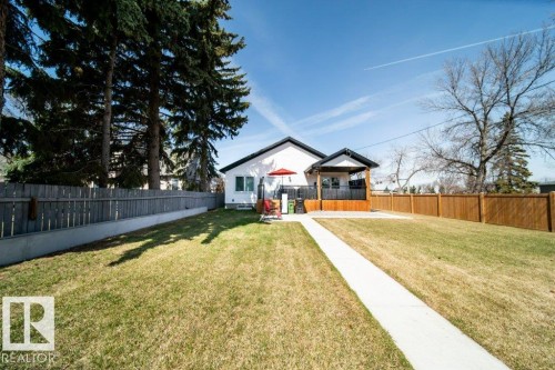 Expansive backyard featuring a manicured lawn, a concrete pathway, a wooden deck with a covered portion, and perimeter fencing - 11303 111 Avenue, Edmonton, AB - Outdoor