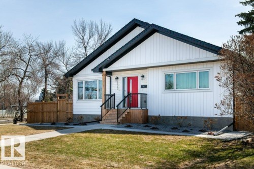 Updated exterior featuring white vertical siding, a striking red front door, black roofline trim, a dark gray shingle roof, and established landscaping - 11303 111 Avenue, Edmonton, AB - Outdoor