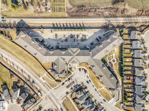 Aerial perspective highlighting a multi-unit residential property with extensive parking, surrounding green spaces, and adjacent residential structures - 322 1520 Hammond Gate Nw, Edmonton, AB - Other