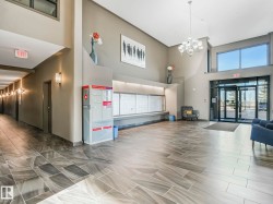 Lobby entrance featuring large format tile flooring, high ceilings, a contemporary chandelier, mailboxes, and a glass-paneled entry door with transom windows - 