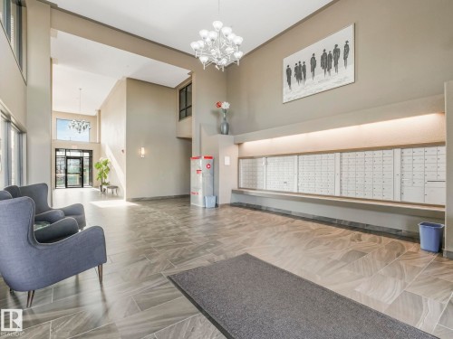Spacious entry lobby featuring high ceilings, large format tile flooring, contemporary chandelier, and built-in mailboxes with accent lighting - 322 1520 Hammond Gate Nw, Edmonton, AB - Indoor Photo Showing Other Room