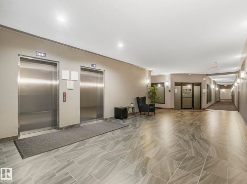 Elevator lobby featuring two stainless steel elevators, overhead recessed lighting, modern sconces, and large format tile flooring - 322 1520 Hammond Gate Nw, Edmonton, AB - Indoor Photo Showing Other Room