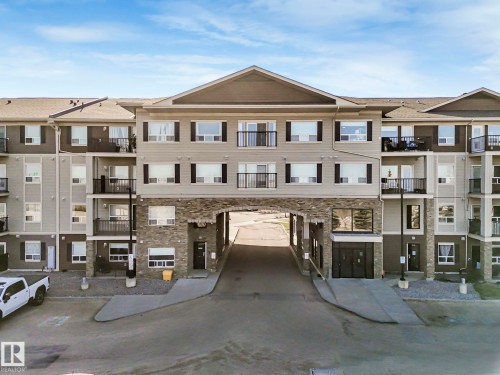 Multi-story building featuring a stone facade at the base, private balconies, and a central drive-through archway - 322 1520 Hammond Gate Nw, Edmonton, AB - Outdoor With Balcony With Facade