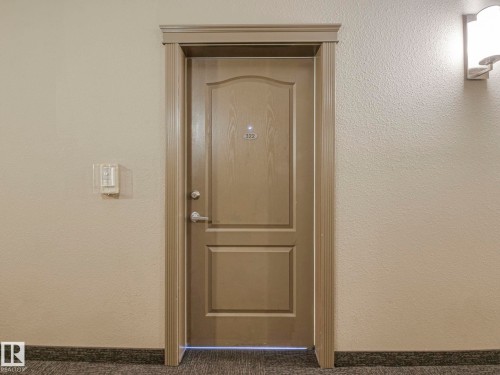 Warm-toned entry door featuring decorative paneling and detailed trim work - 322 1520 Hammond Gate Nw, Edmonton, AB - Indoor
