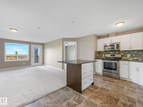Open-concept living space featuring a kitchen island with storage, stainless steel appliances, white cabinetry, a glass tile backsplash, and a window and door providing outdoor access - 322 1520 Hammond Gate Nw, Edmonton, AB - Indoor Photo Showing Kitchen With Upgraded Kitchen