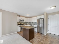 Kitchen featuring white cabinetry, stainless steel appliances, a multi-tone tile backsplash, and a central island with a dark countertop - 