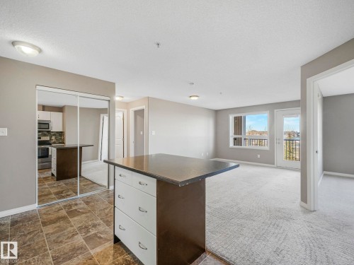 Open-concept living area featuring a kitchen island with drawers, expansive mirrored closet doors, a large window, and a glass-paneled door leading to an exterior balcony - 322 1520 Hammond Gate Nw, Edmonton, AB - Indoor