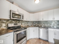 Modern kitchen featuring white cabinetry, stainless steel appliances, dark countertops, a mosaic tile backsplash, and tile flooring - 