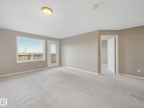 Carpeted living space featuring a window with a black railing, a door with glass panels, painted walls, and white trim - 322 1520 Hammond Gate Nw, Edmonton, AB - Indoor Photo Showing Other Room