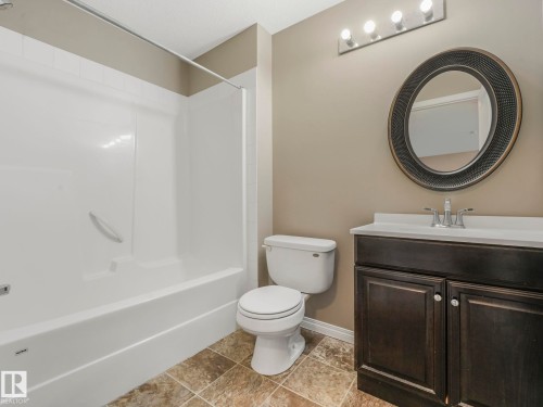 Bathroom featuring a white bathtub/shower combination, dark wood-finish vanity with a white countertop, and an oval mirror with textured frame - 322 1520 Hammond Gate Nw, Edmonton, AB - Indoor Photo Showing Bathroom