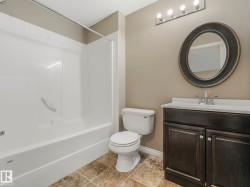 Bathroom featuring a white bathtub/shower combination, dark wood-finish vanity with a white countertop, and an oval mirror with textured frame - 
