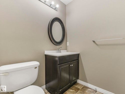 Bathroom featuring a dark wood-finish vanity with a white countertop, an oval mirror, a three-light vanity fixture, and tiled flooring - 322 1520 Hammond Gate Nw, Edmonton, AB - Indoor Photo Showing Bathroom