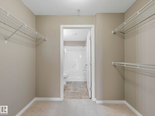 Walk-in closet with carpet flooring, light neutral paint, white wire shelving, and white baseboards - 322 1520 Hammond Gate Nw, Edmonton, AB - Indoor With Storage