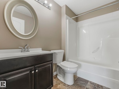 Bathroom featuring a dark wood-finish vanity, white countertop, chrome faucet, and a round decorative mirror - 322 1520 Hammond Gate Nw, Edmonton, AB - Indoor Photo Showing Bathroom