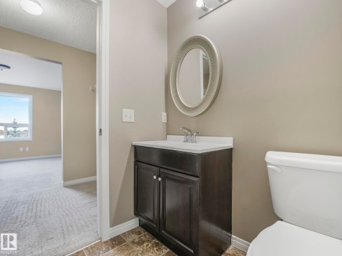 Vanity with a white countertop and base cabinet, complemented by an oval mirror with a decorative frame - 322 1520 Hammond Gate Nw, Edmonton, AB - Indoor Photo Showing Bathroom
