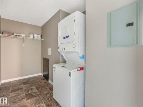 Laundry area featuring a stacked washer and dryer, tile flooring, and overhead wire shelving - 322 1520 Hammond Gate Nw, Edmonton, AB - Indoor Photo Showing Laundry Room
